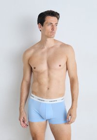 Boxer-briefs bleu clair avec un ajustement près du corps et une taille élastique blanche portant le logo Lacoste. Le tissu semble lisse et doux.