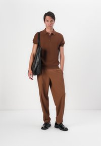 Pólo de malha castanho com mangas curtas e fecho éclair, combinado com calças largas castanhas. Bolsa de ombro de pele preta e sapatos.