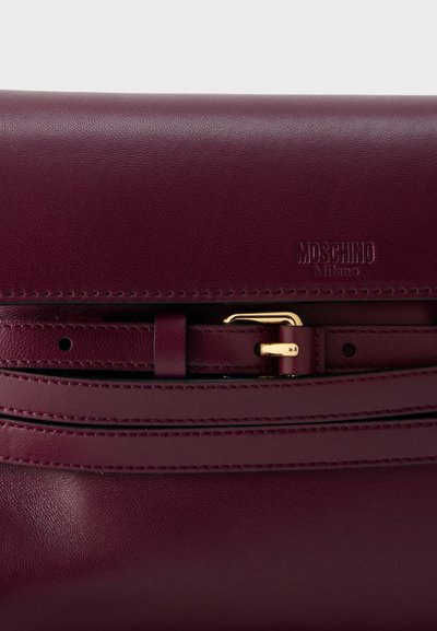 Σκούρα μπορντό δερμάτινη τσάντα με ραμμένη ζώνη και μικρή χρυσή αγκράφα, με ανάγλυφο λογότυπο "Moschino Milano".