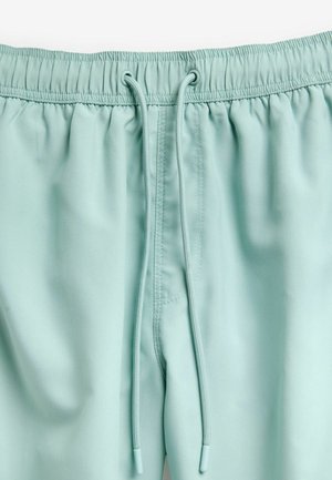 Helle mintgrüne Shorts aus weichem Material, mit einem elastischen Bund mit Kordeln und seitlichen Taschen. Glatte Textur mit minimalen Nähten.