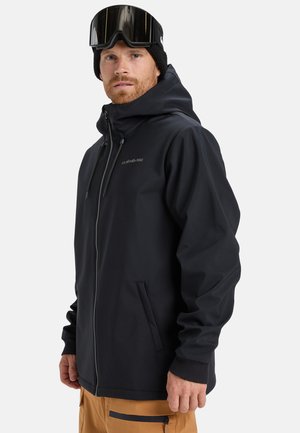 Veste d'extérieur noire avec capuche à cordon de serrage, fermeture éclair à l'avant et deux poches latérales. Poignets extensibles et tissu lisse et élégant. Lunettes de neige portées.