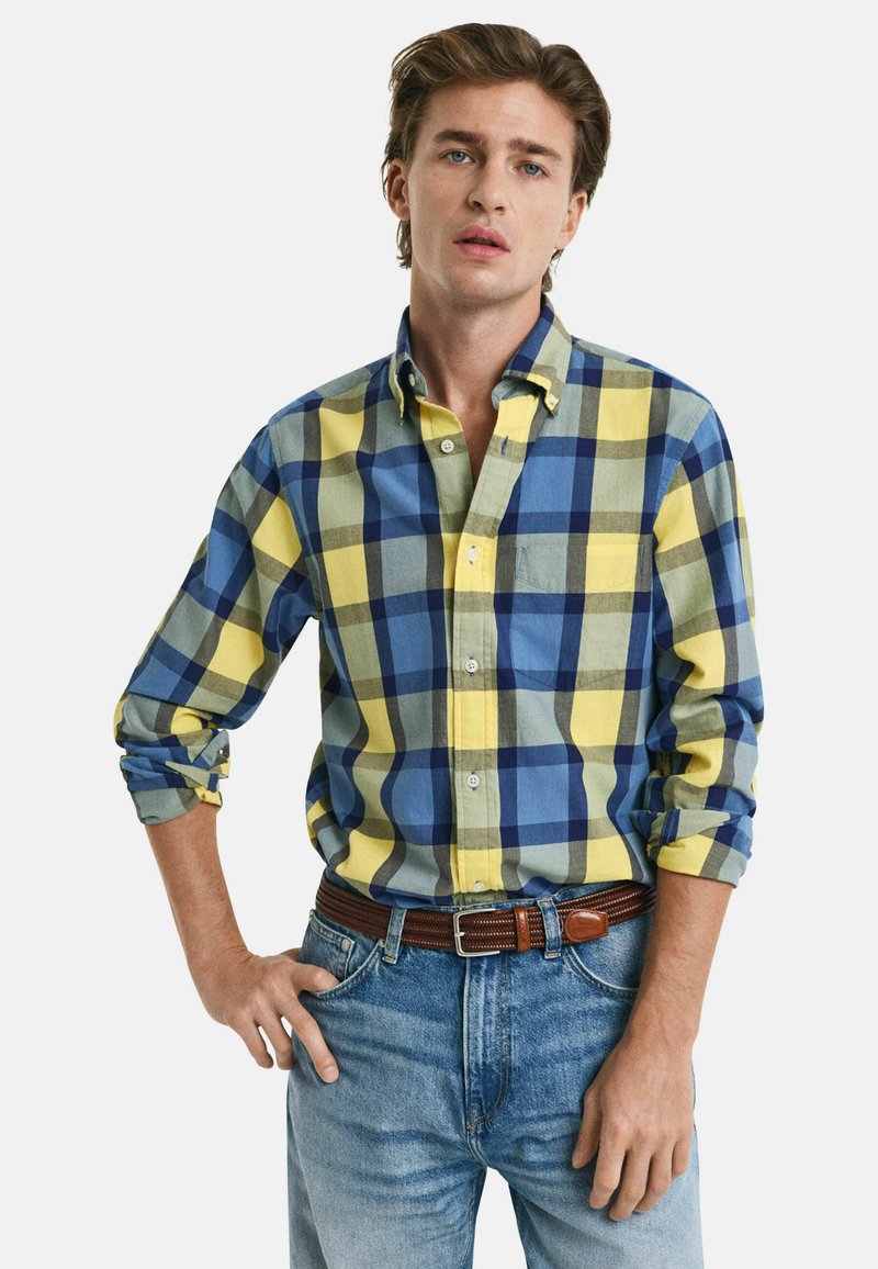 Hemd mit Kragen im Karomuster in Gelb, Blau und Grün. Lange Ärmel hochgekrempelt, lässige Passform, kombiniert mit blauen Jeans und einem braunen Gürtel.