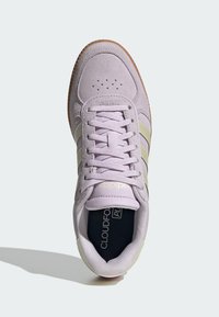 Fioletowy zamszowy but sportowy z trzema zielonymi paskami, teksturowanym językiem i miękką wkładką. Posiada nadrukowane logo na języku oraz gumową podeszwę.