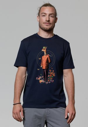 Navyblauwe T-shirt met een speelse afbeelding van een aangeklede giraffe in een pak met bloemen, vlinders en een wandelstok, gedrukt in levendige kleuren.