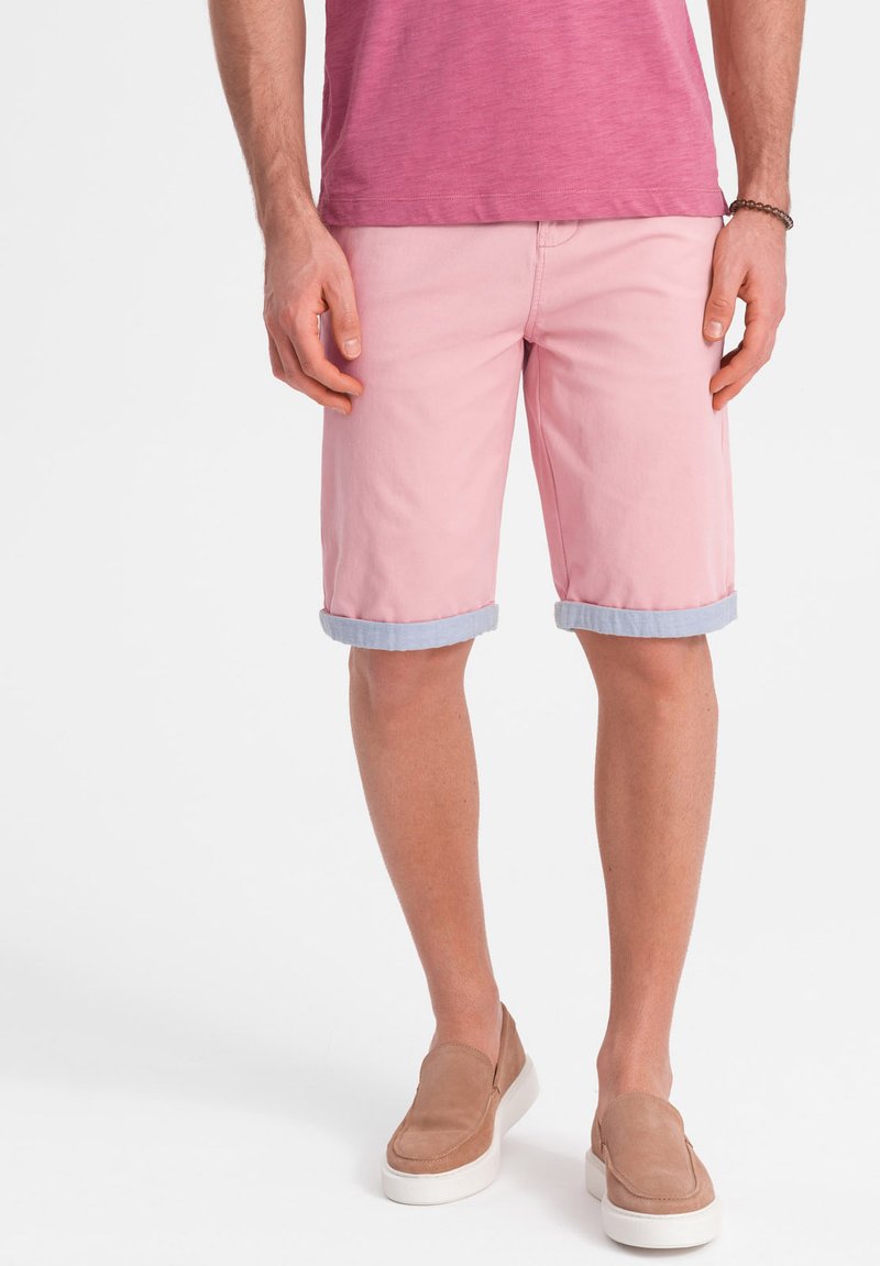 Růžové bavlněné šortky s ohrnutými manžetami, předními kapsami a světle modrým lemem. V kombinaci s tričkem s krátkým rukávem z texturovaného materiálu v světlé růžové barvě a béžovými nazouvacími botami.