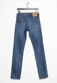 Jean en denim bleu avec une coupe droite, doté d'une étiquette de marque en cuir marron, cinq poches et des détails de coutures discrètes.