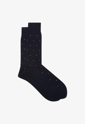 Par de calcetines negros de caña con pequeño patrón de puntos blancos y puños acanalados, colocados planos sobre fondo blanco.
