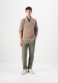Beige gerippter Pullover mit einem Viertelreißverschluss-Kragen, kombiniert mit olivgrünen Hosen und beigen Sneakers. Einfaches, sauberes Design mit subtilen Texturen.