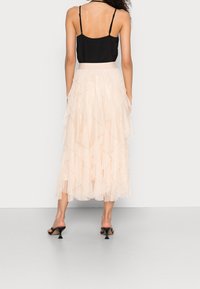 Haut noir à fines bretelles associé à une jupe en tulle rose pâle à couches. La jupe présente un design à volants et une longueur mi-mollet. Sandales à talons noires.