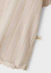 Tessuto rosa chiaro con strisce verticali, caratterizzato da bordi a scallop e delicate cuciture. Include un piccolo etichetta beige con la scritta "Lil' Atelier."