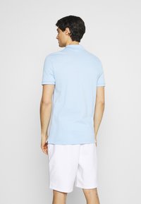 Polo azzurro chiaro in cotone, con colletto classico e maniche corte, abbinato a pantaloni corti bianchi. Texture liscia, design semplice.