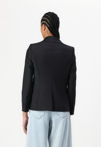 Černý přizpůsobený blazer se strukturovaným střihem, s klopami a zapínáním na knoflíky na manžetách. Nosený přes světle modré �široké džíny. Hladký povrch tkaniny.