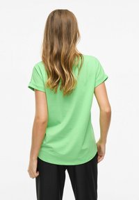 Grön kortärmad T-shirt med rullade ärmar, tillverkad av mjukt bomullsmaterial. Rundad nederkant och avslappnad passform. Bärs tillsammans med svarta byxor.