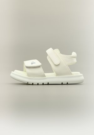 Witte kindersandaal met twee verstelbare klittenbandsluitingen en een gewatteerde zool, afgebeeld tegen een neutrale achtergrond.
