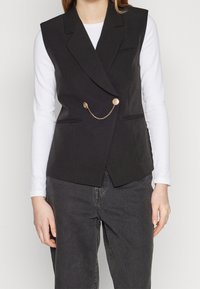 Svart ärmlös blazer med skräddarsydd passform, utrustad med två framfickor med klapp och en guldkedjeaccent med runda knappar.