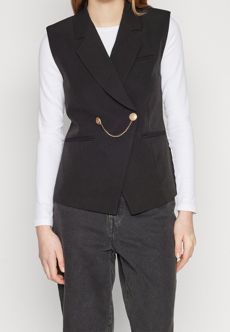 Svart ärmlös blazer med skräddarsydd passform, utrustad med två framfickor med klapp och en guldkedjeaccent med runda knappar.