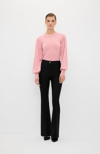 Roze blouse met lange mouwen en opgeblazen schouders, gecombineerd met hoge zwarte flare-broek met een knoopdetails aan de voorkant en een gladde textuur.
