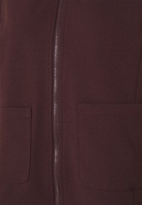 Maroon zip-up jacket featuring two front pockets, soft fabric texture, and a streamlined design. Front zipper runs vertically along the center.