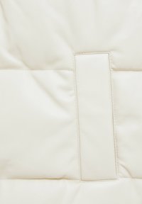 Gros plan d'une tapisserie en cuir matelassé ivoire avec un détail de couture rectangulaire et une texture lisse, légèrement froissée.