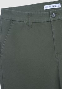 Oliwkowe bawełniane spodnie z zapięciem na guzik, szlufkami na pasek oraz ukośnymi przednimi kieszeniami. Gładka tekstura, dopasowany krój i staranne detale szycia.