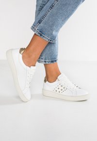 Vita lädersneakers med guld accenter och stjärnformade utskärningar, med en texturerad vit sula och platta snören. Bärs med cropped jeans.