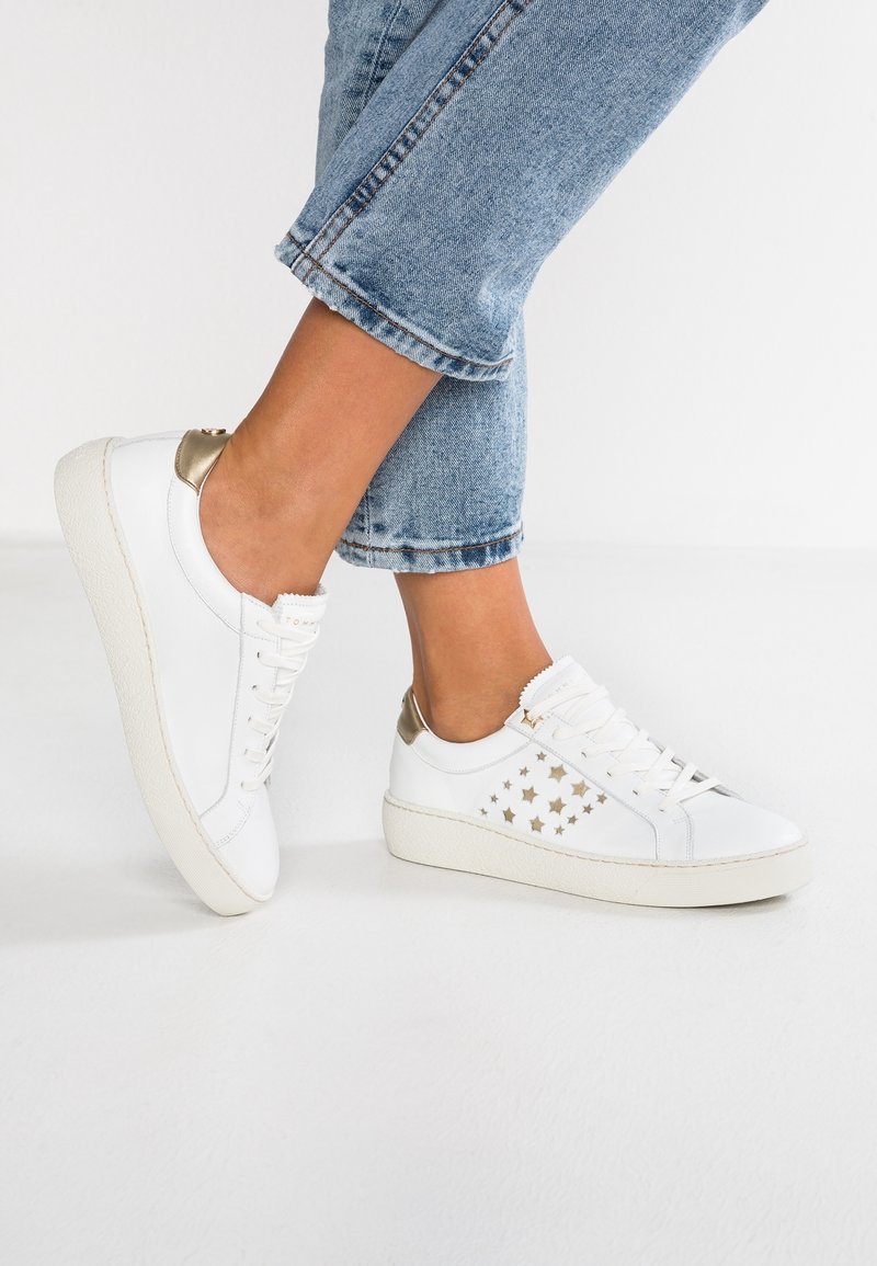 Vita lädersneakers med guld accenter och stjärnformade utskärningar, med en texturerad vit sula och platta snören. Bärs med cropped jeans.