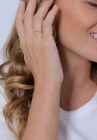 Anillo de banda de diamantes con pequeños diamantes redondos engastados en una banda de plata pulida, llevado en el dedo de una mujer sobre un fondo claro.