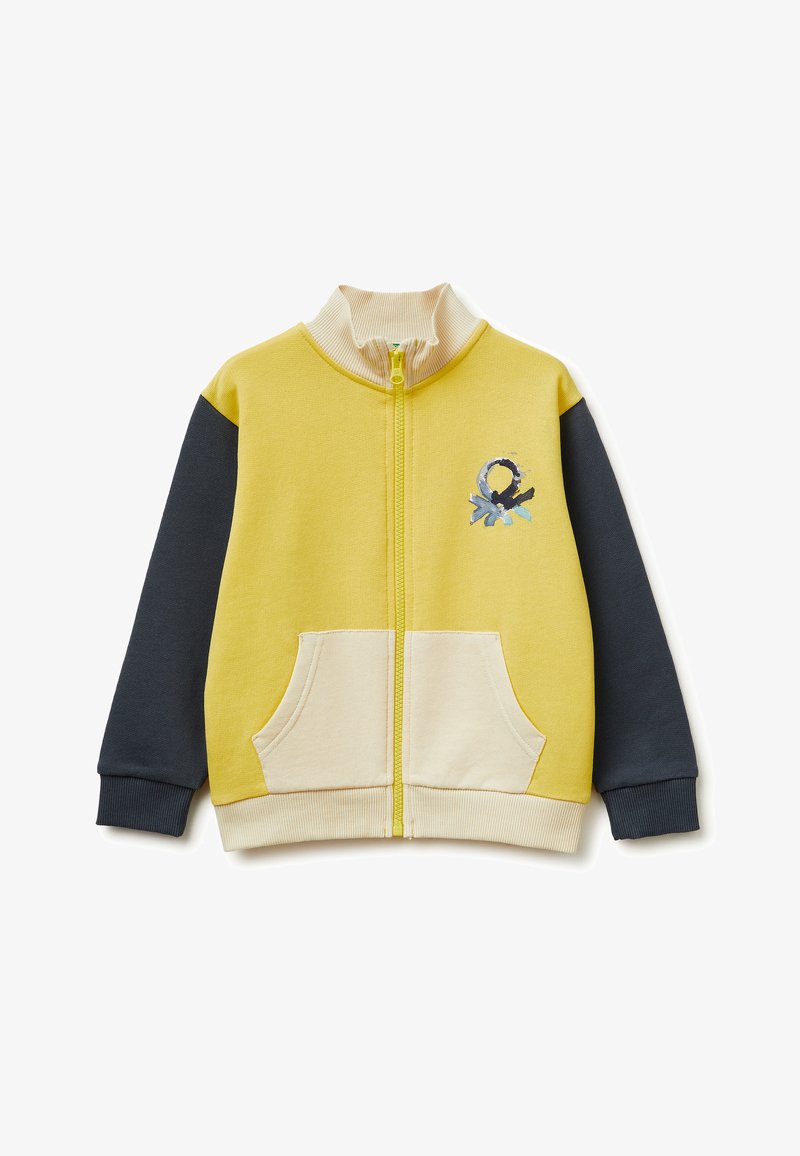 Kinderjas met rits, gele voorkant en achterkant, donkergrijze mouwen, beige geribbelde kraag en zakken, en een klein abstract logo op de borst.