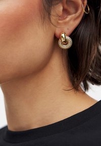 Guldörhängen i form av en cirkel med små klara ädelstenar. Släta och texturerade ytor skapar visuell kontrast.