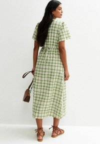 Grün-weiß karierte Midi-Kleid mit kurzen Puffärmel, tailliertem Schnitt und Bindeband im Rücken. Kombiniert mit braunen Riemchensandalen und einer kleinen Tasche.