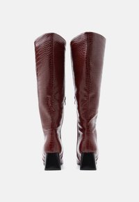 Μποτάκια μπορντό μέχρι το γόνατο με τακούνι, κατασκευασμένα από γυαλιστερό τεχνητό δέρμα κροκόδειλου, με τετράγωνο μαύρο τακούνι και λεία υφή.