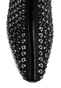 Czarny płaski but z zaokrąglonym noskiem, ozdobiony okrągłymi srebrnymi ćwiekami ułożonymi w rzędy. Gładka faktura materiału z centralnym szwem.