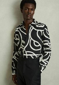 Camicia button-up a righe bianche e nere con vortici astratti, maniche lunghe e colletto classico, abbinata a pantaloni neri su misura.
