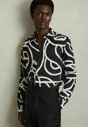 Camicia button-up a righe bianche e nere con vortici astratti, maniche lunghe e colletto classico, abbinata a pantaloni neri su misura.