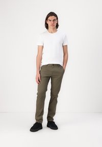 Hvid kortærmet t-shirt kombineret med olivengrønne lige ben-bukser. Modellen har sorte sko på og står foran en ensfarvet baggrund.