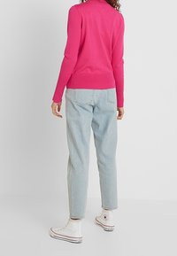 Enganliegender, heißrosa Pullover mit langen Ärmeln und geripptem Saum, kombiniert mit hellblauen, lässig geschnittenen Jeans und weißen High-Top-Sneakern.