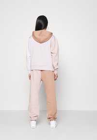 Hooded sweatshirt in light pink and beige with a relaxed fit, paired with matching beige sweatpants. Smooth texture, elastic cuffs, and hem.