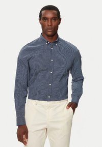 Camisa de cuadros azul marino con cuello extendido, mangas largas y botones blancos, combinada con pantalones claros.