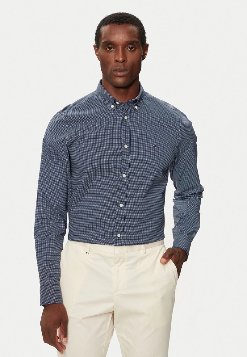 Camisa de cuadros azul marino con cuello extendido, mangas largas y botones blancos, combinada con pantalones claros.