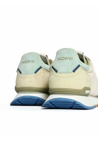 Zapatillas beiges y verdes con un empeine de ante texturizado, que cuentan con una suela de goma azul y el logo "HOFF" grabado en el talón.