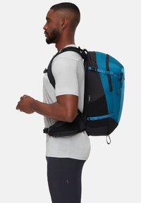 Ryggsäcken har en svart och blå design med en vadderad rygg, justerbara remmar och flera fack. Materialet verkar hållbart och strukturerat.