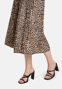 Spódnica plisowana w panterkę w odcieniach beżu i czerni, zestawiona z czarnymi sandałami na obcasie z odkrytymi palcami, które mają szerokie paski i kwadratowy obcas.