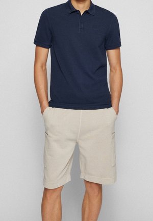Marineblaues Poloshirt mit Dreiknopfleiste und gesticktem Logo, kombiniert mit hellbeigen Cargo-Shorts mit Seitentaschen.