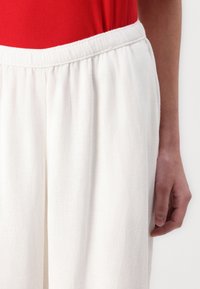 Vita linnebyxor med elastisk midja och mjukt material, kombinerat med en röd topp som visar en avslappnad design.