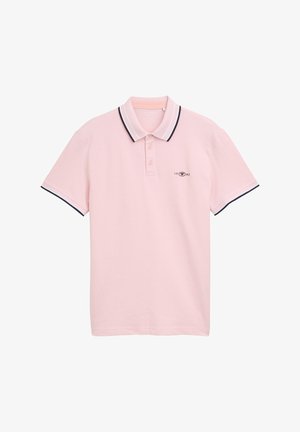 Polo shirt rose pâle en coton avec un col à trois boutons. Il présente un col et des poignets ribbés bleu marine, ainsi qu'un petit logo avec le détail "1962".