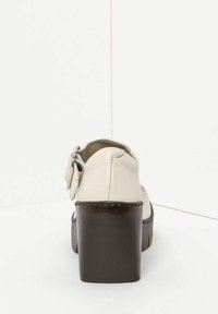 White leather platform shoe with a thick black heel, featuring a buckle accent on the side and a smooth texture.