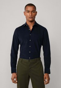 Navy blauwe button-up shirt met een gladde textuur, getailleerd ontwerp en contrasterende lichtblauwe kraag, gecombineerd met olijfgroene broeken.
