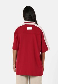 Rode polo shirt met witte zijaccenten en een klein label op de achterkant. Korte mouwen, relaxte pasvorm, gemaakt van een soepele stof.