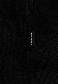 Sort strikket stof med et struktureret mønster. Inkluderer et lille, rektangulært mærke med "JACK&JONES" i hvid tekst.