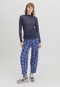 Langärmliges, dunkelblaues Oberteil mit einer taillierten Passform, kombiniert mit lockeren, floral gemusterten blauen Hosen. Graue Sneaker mit rosa Akzenten runden das Outfit ab.